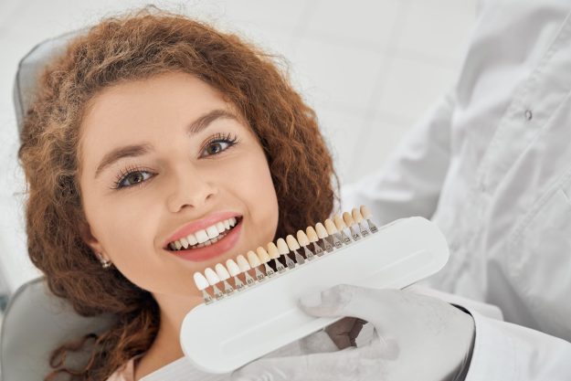 Woman smiling while male dentist keeping teeth color range Tooth Bonding Transformations